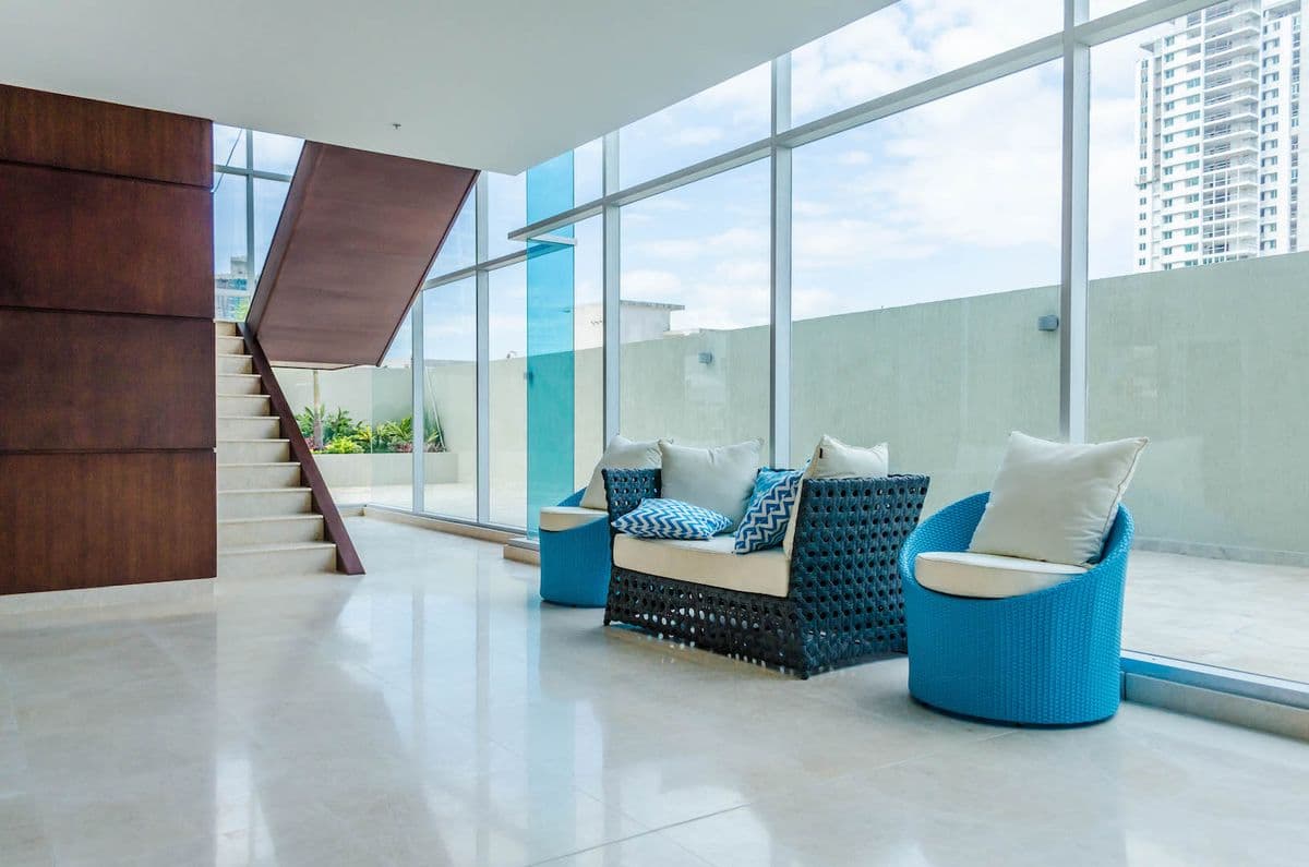 Glass-walled lounge with a staircase and blue armchairs at The Palace