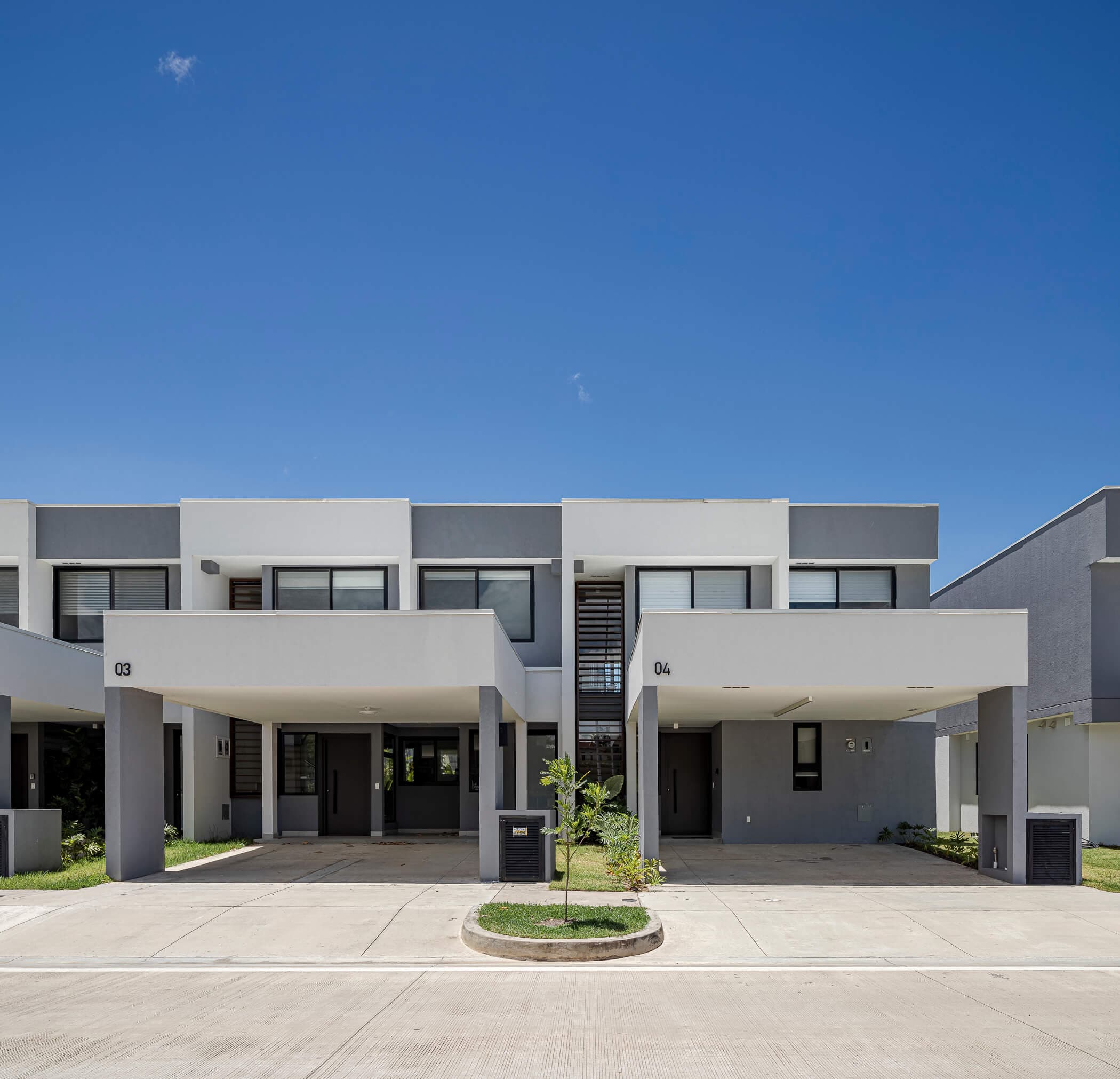 Pair of Imaterra townhomes with covered parking under a blue sky