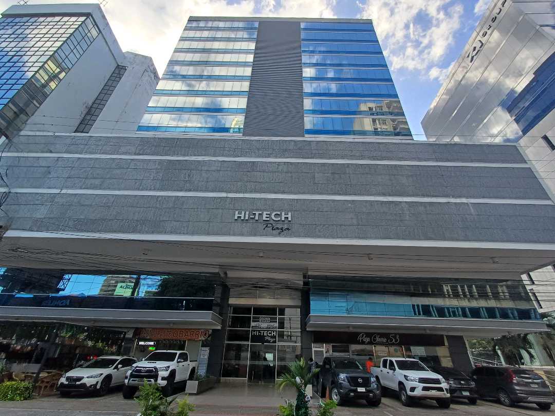Facade of the Hi-Tech Plaza office building with its glass tower above the stone-clad podium and name sign, Obarrio, Panama City