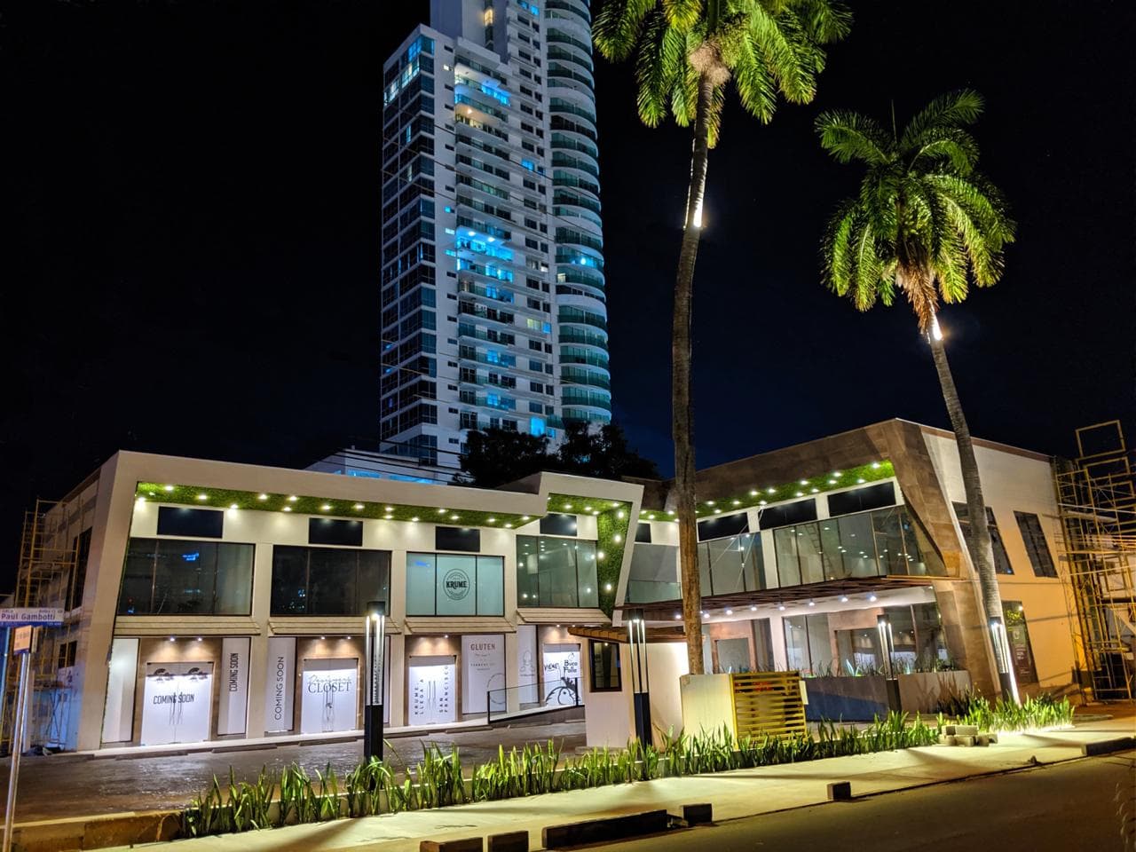 Color night view of the Plaza Corner 68 storefronts with palm trees and the tower behind, San Francisco, Panama City