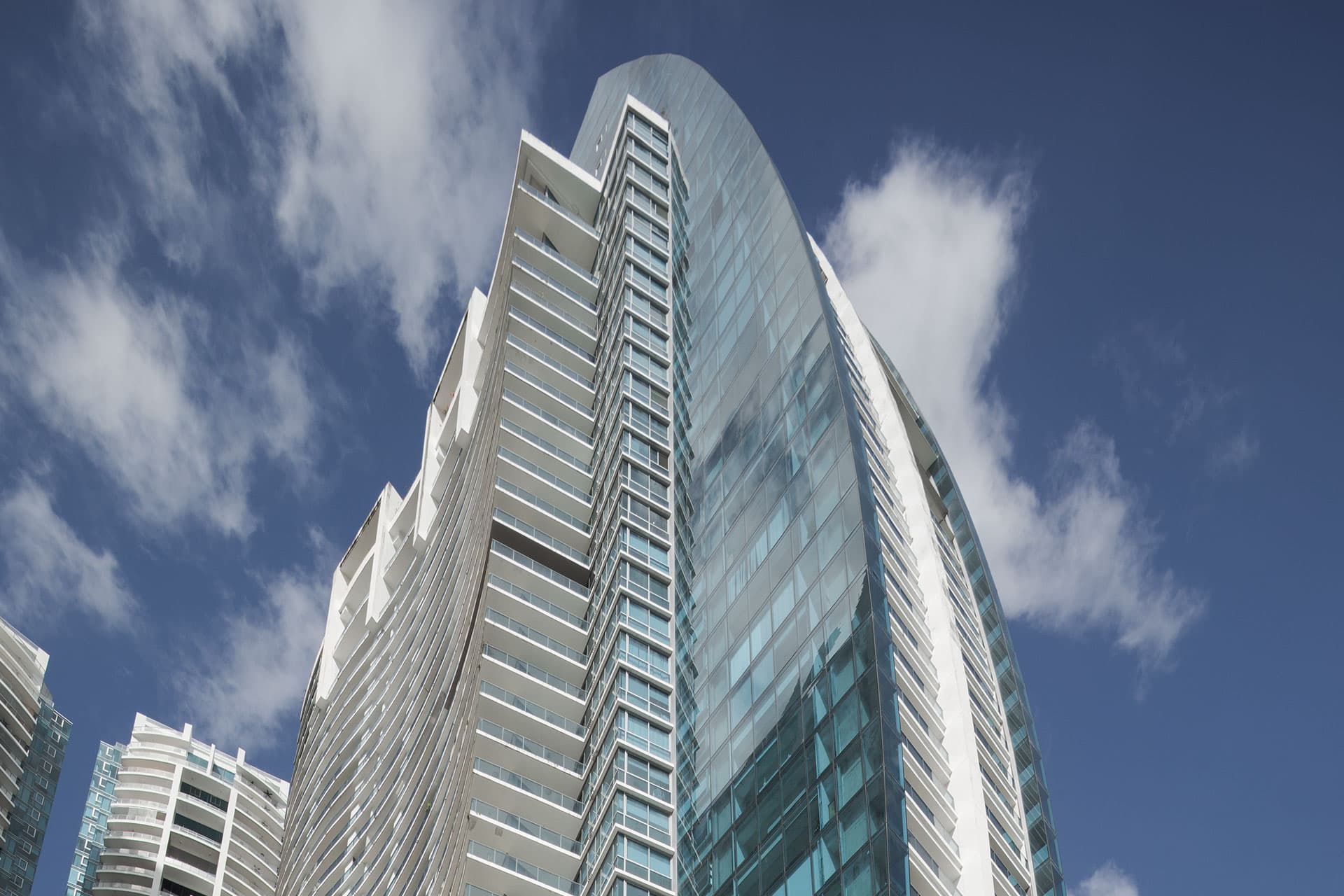 Curved glass and white facade of Grand Tower against a blue sky in Punta Pacifica