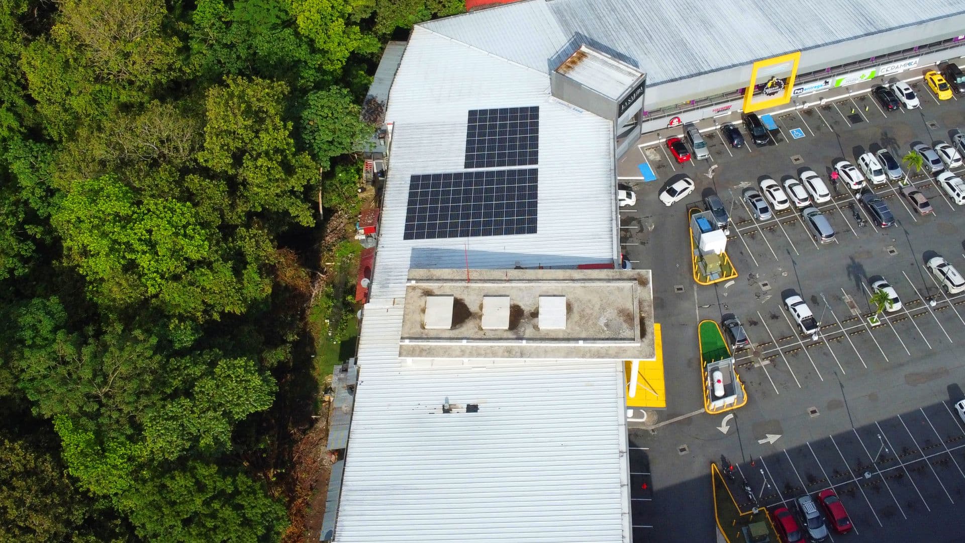 Aerial view of Brisas Mall's rooftop solar panels and parking beside the woods of Brisas del Golf