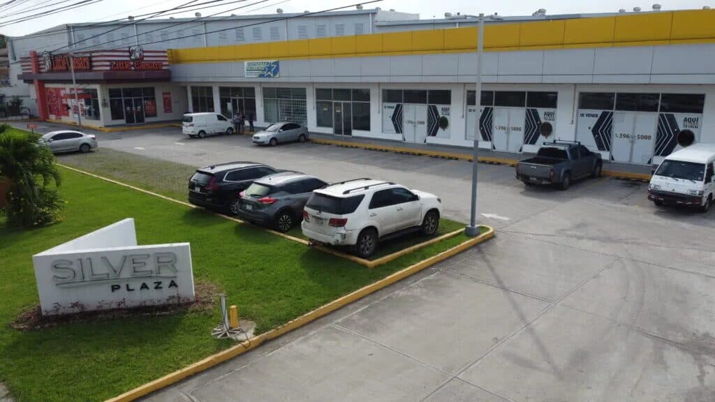 Front of Silver Plaza with its sign, yellow-banded retail units and parking in Las Mañanitas