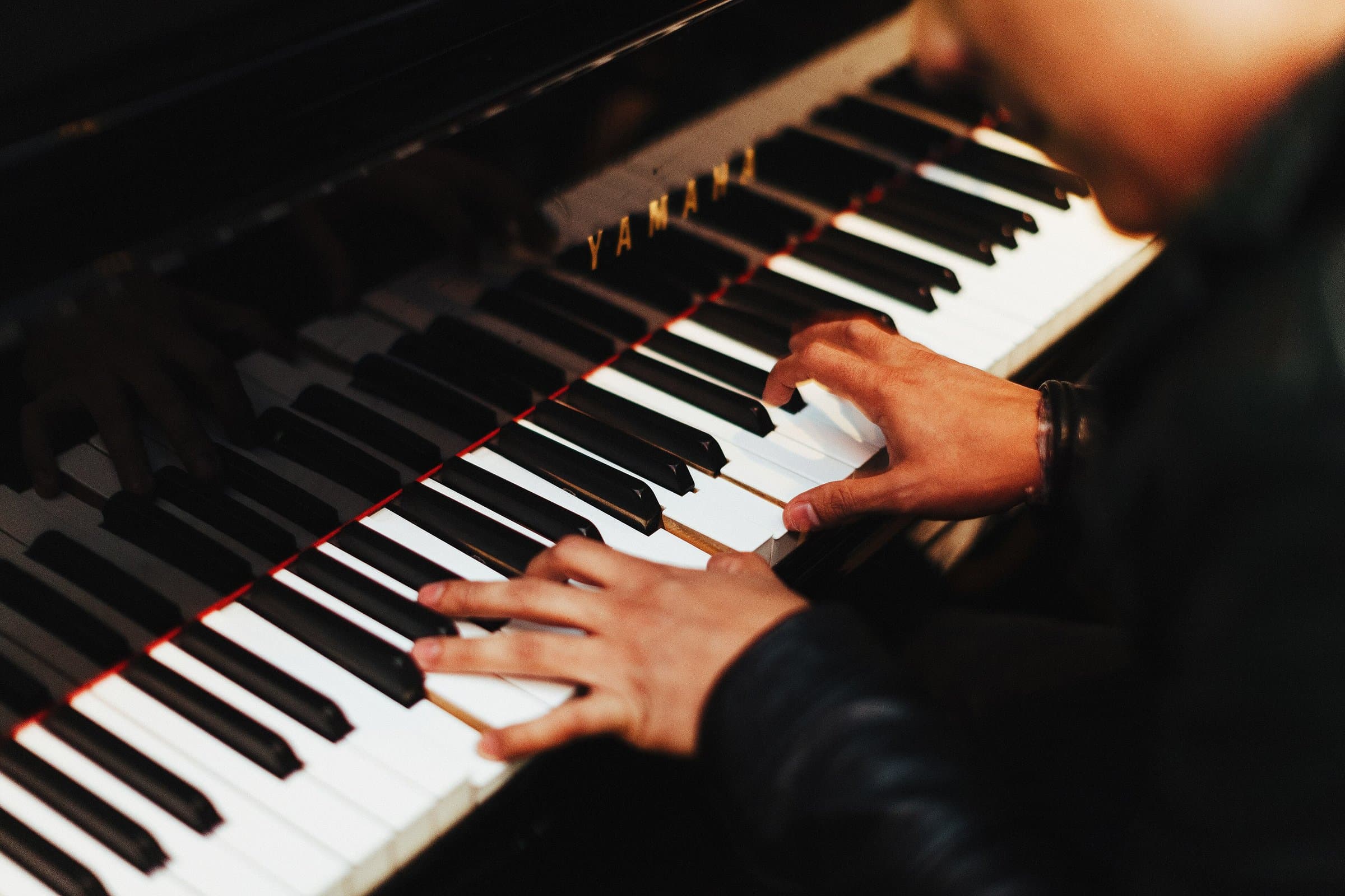 Pianist's hands on the keys of a black piano in warm, dim lighting