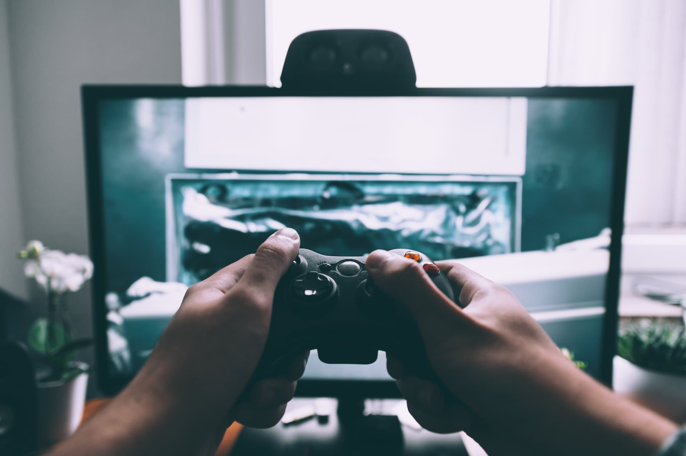 Hands holding a video game controller in front of a large gaming monitor
