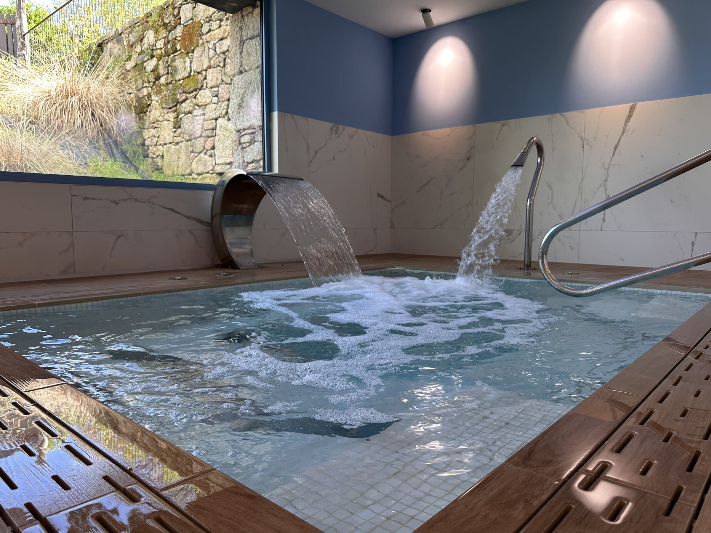 Indoor jacuzzi with a waterfall spout and a water jet bubbling into the pool, framed by marble walls