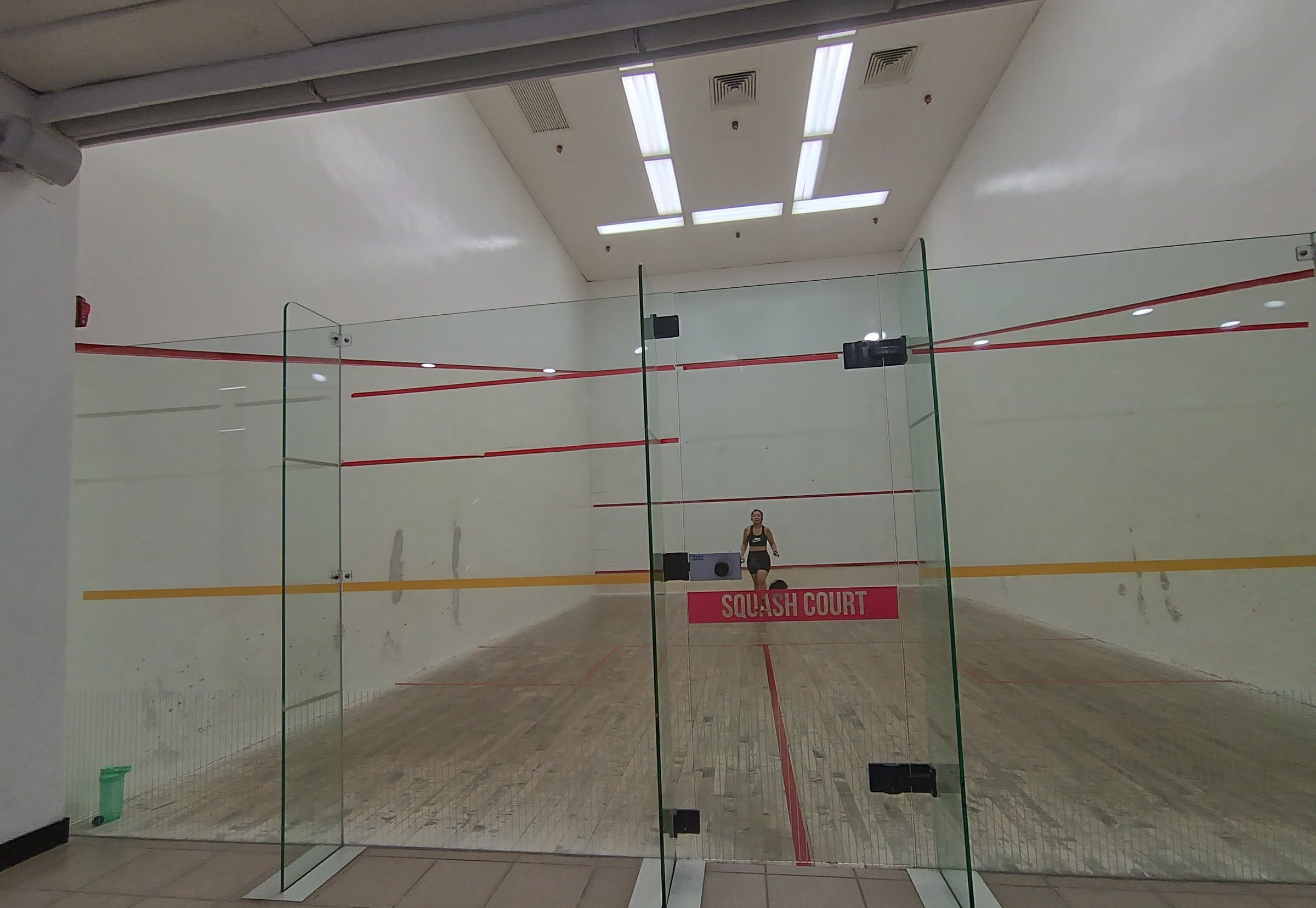 Glass-walled squash courts with white walls and red boundary lines in a sports centre