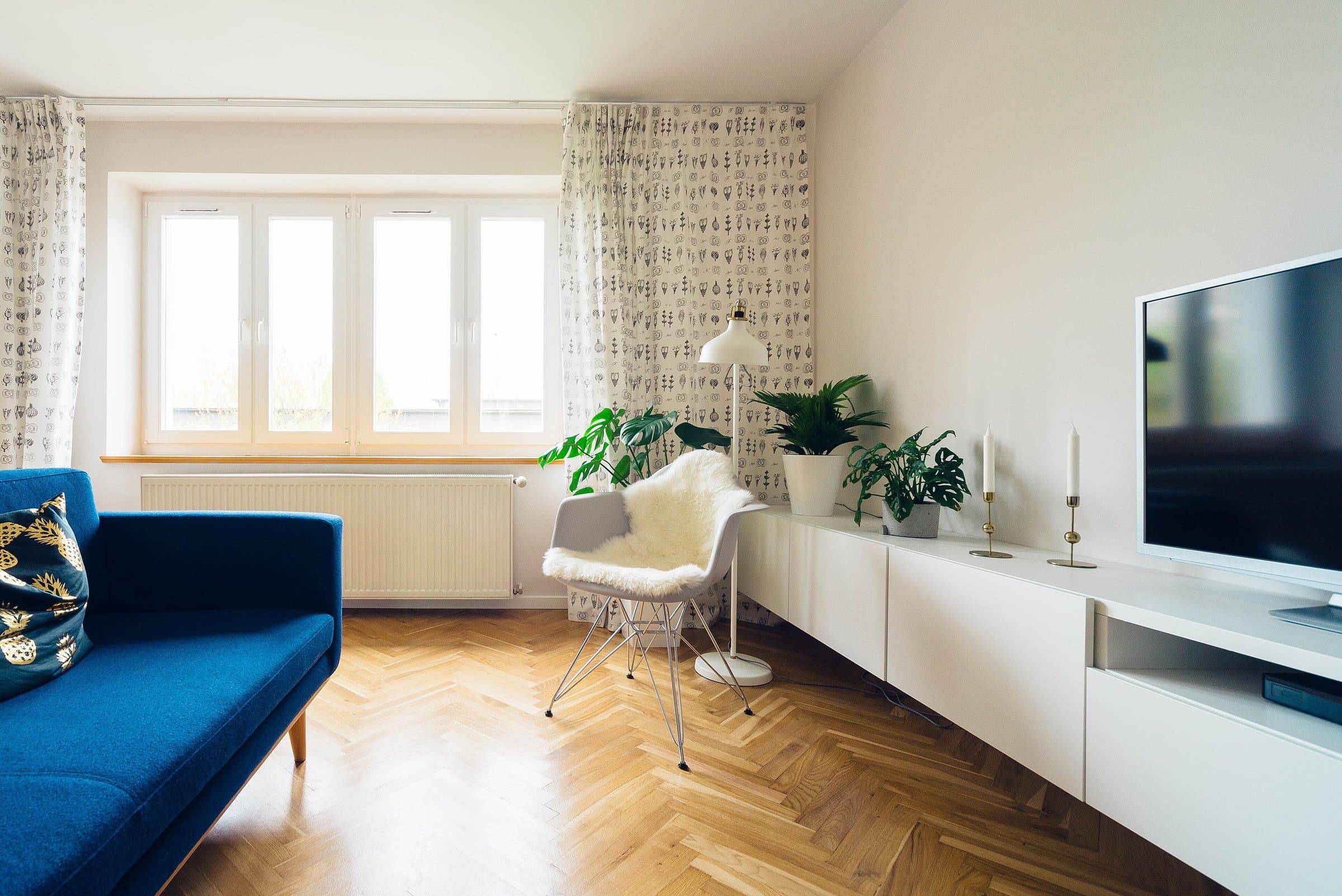 Bright furnished living room with a blue sofa, a white armchair, house plants and a television