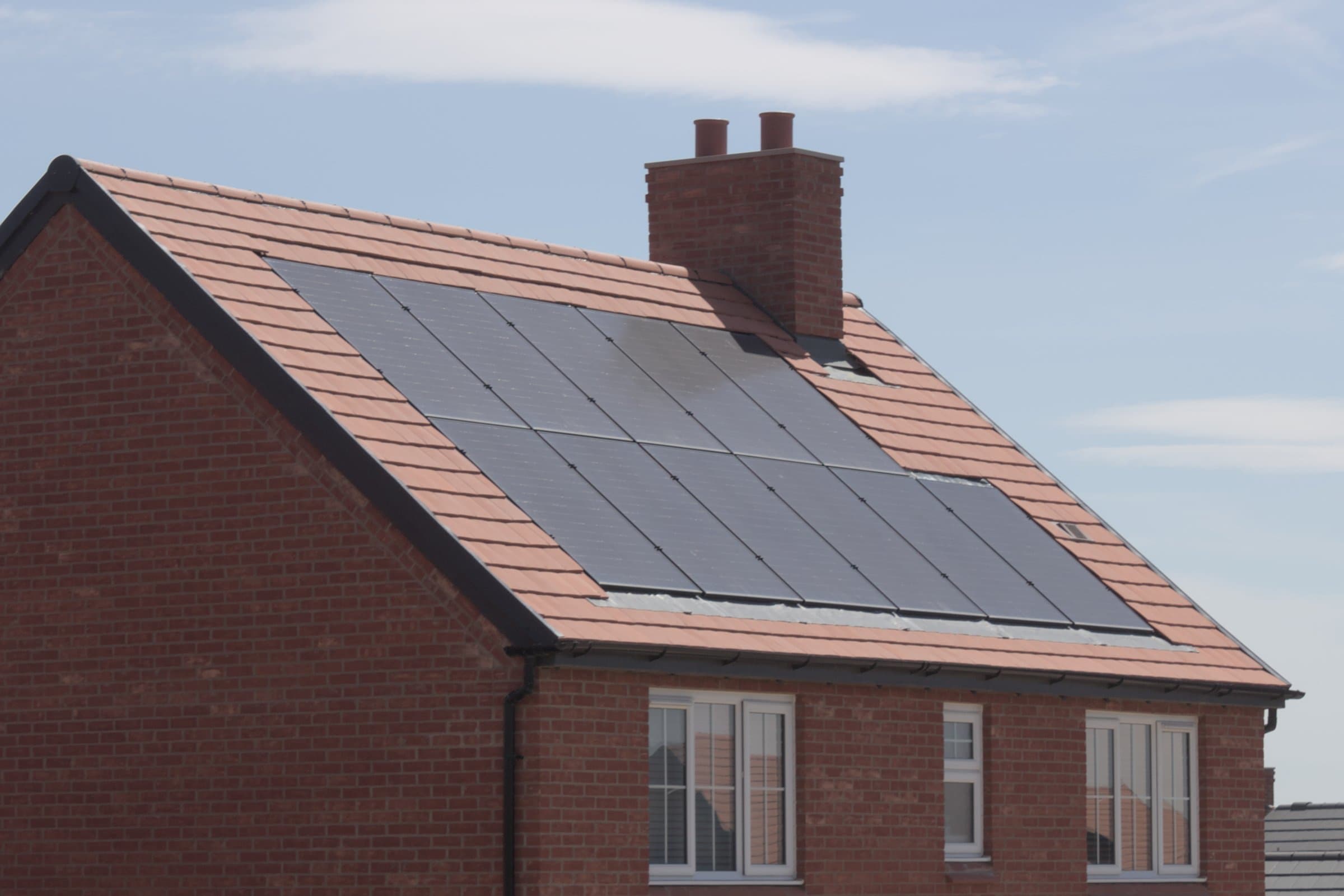 Solar panels installed on the tiled roof of a brick house under a clear sky