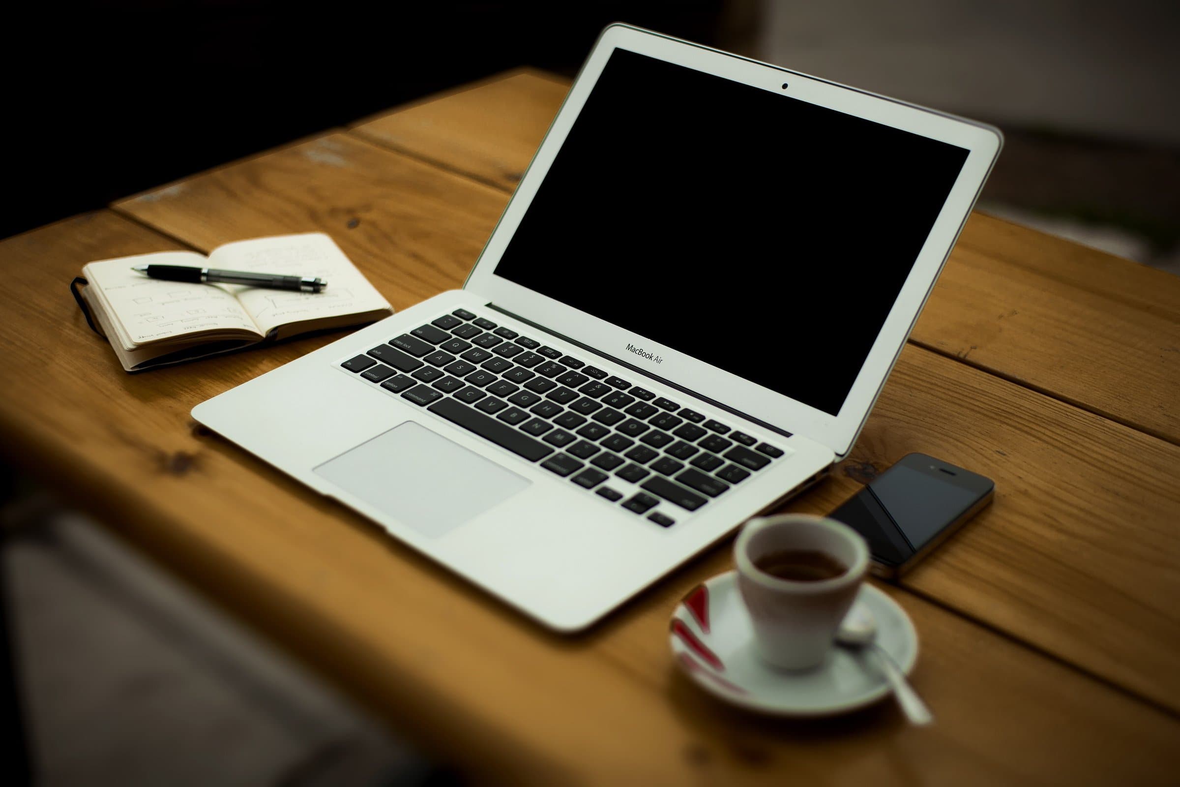 Laptop, open notebook, smartphone and a cup of coffee on a wooden desk