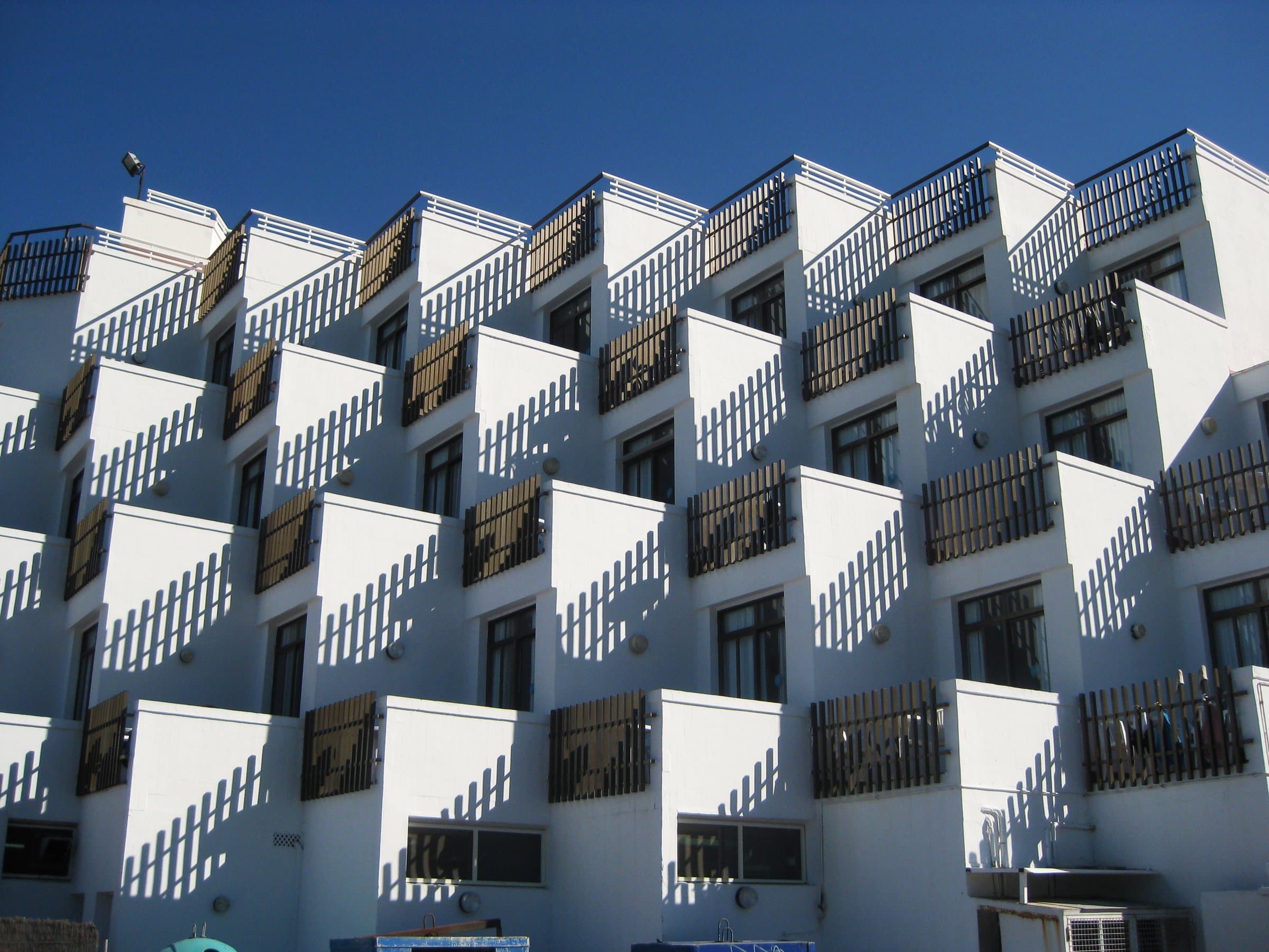 White apartment building with stepped cubic terraces and wooden railings under a blue sky