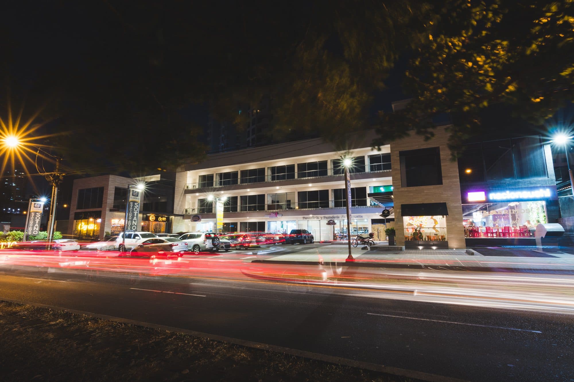 Plaza El Cangrejo storefronts at night with passing traffic