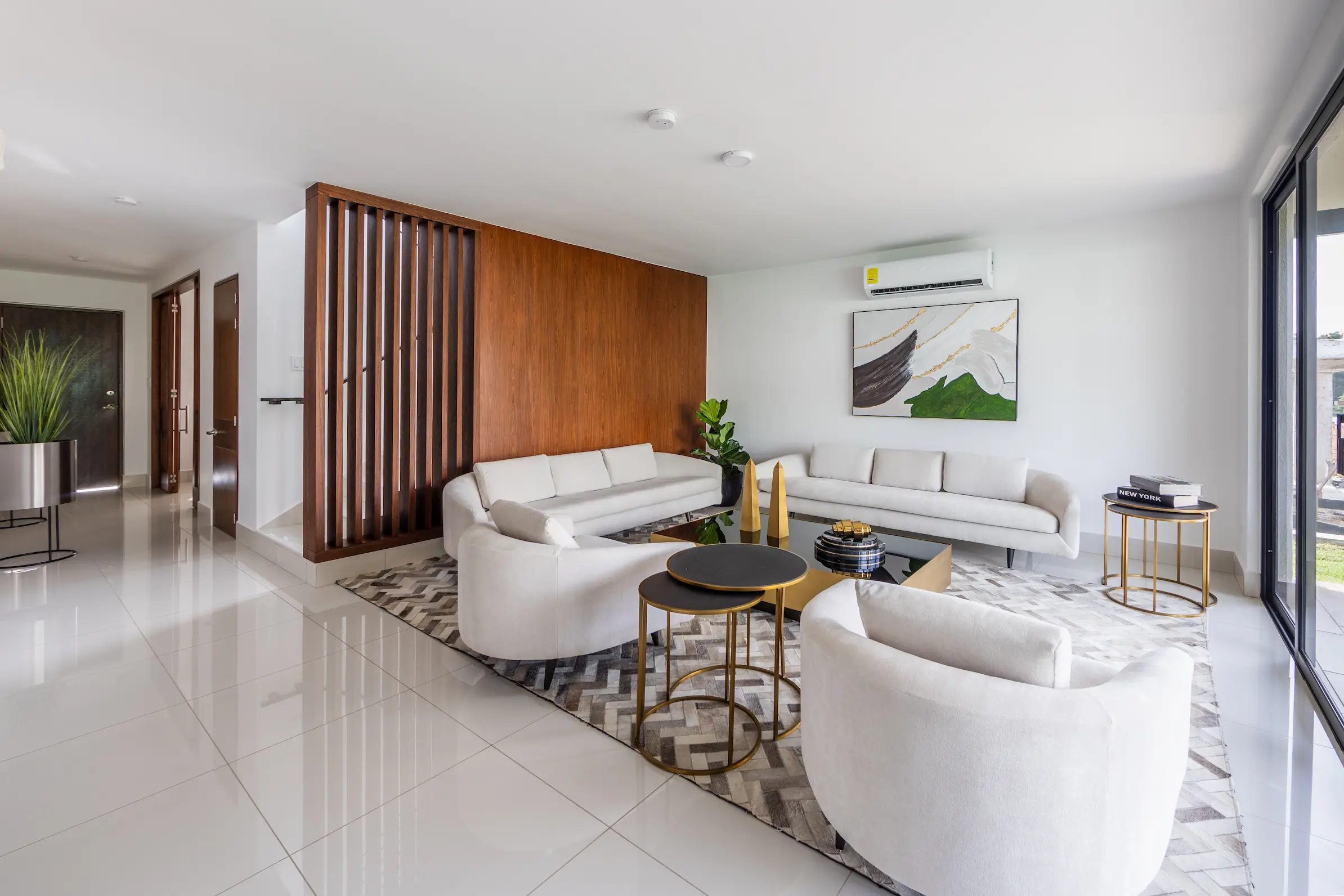Living room with white armchairs and a wood-slat divider in an Arcadia model house, Costa Verde