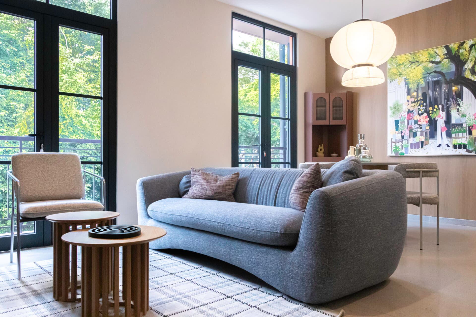 Living room with a gray sofa and tall windows to the trees in a La Quince apartment