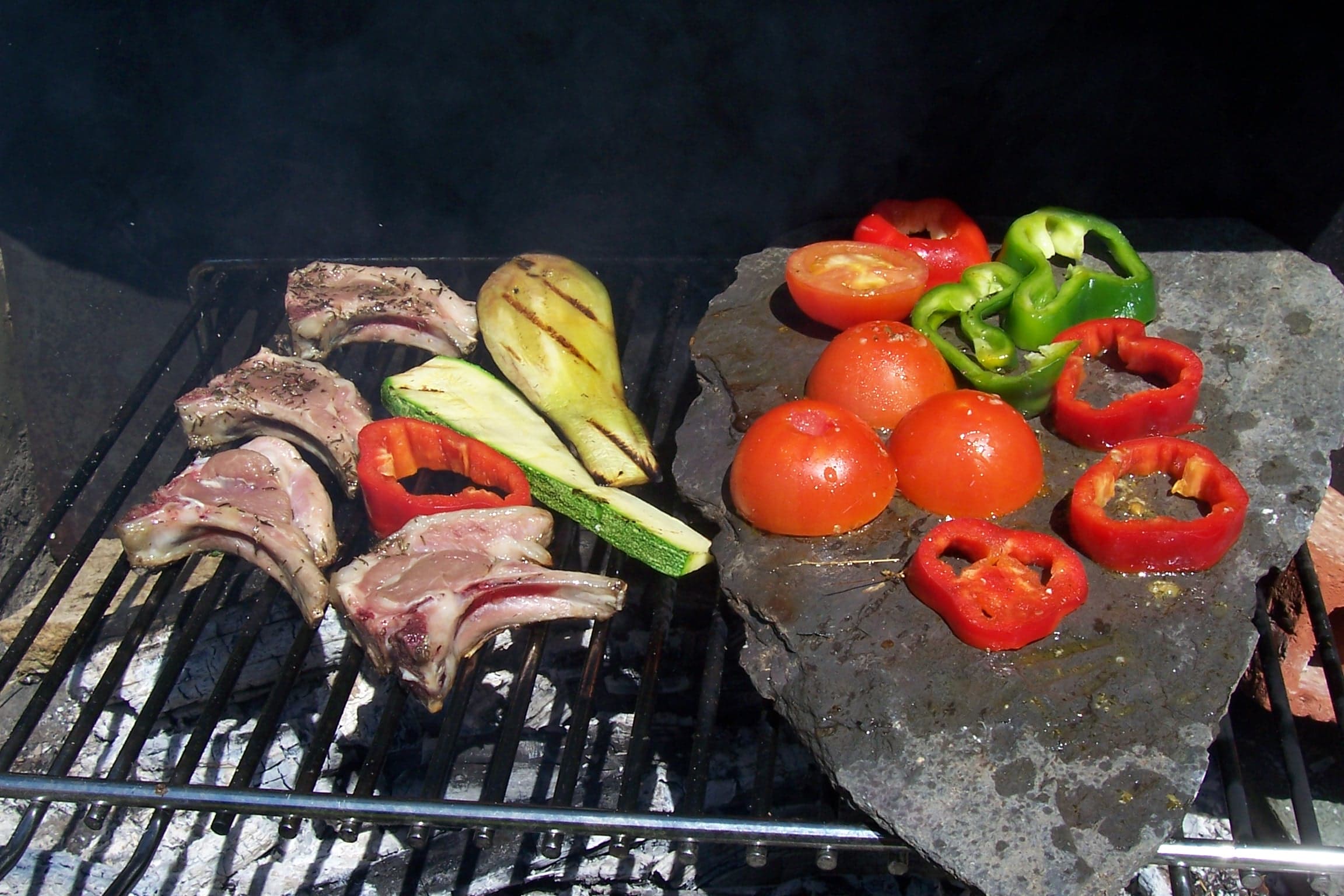 Chops, zucchini, tomatoes and peppers cooking on a charcoal barbecue grill and on a hot stone