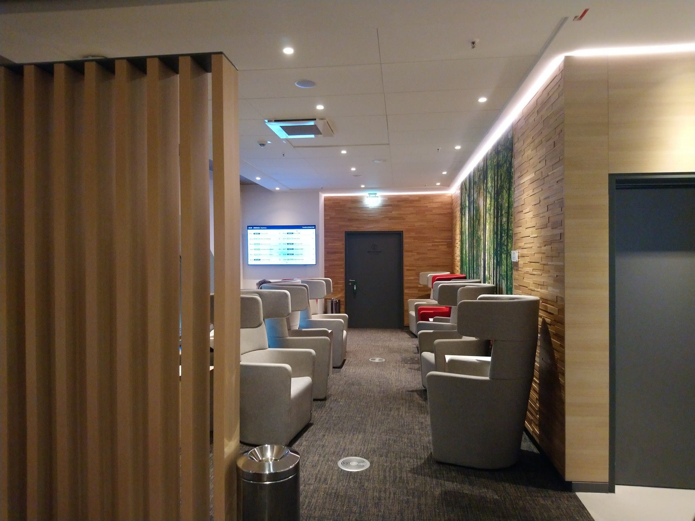 Lounge area with rows of upholstered armchairs, a wood-slat screen and a wood-clad wall under soft lighting