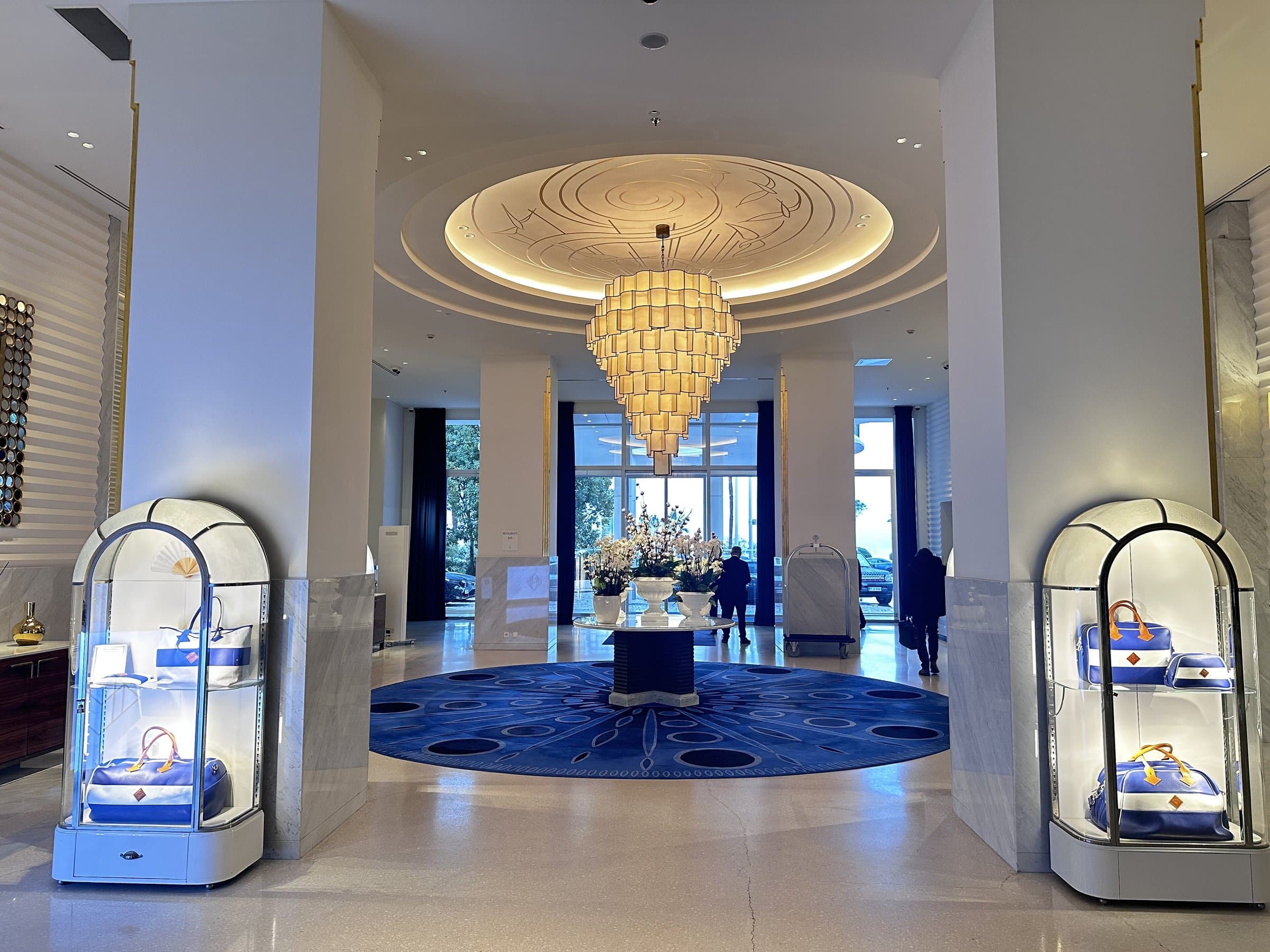 Grand lobby with a chandelier, brass luggage trolleys and tall windows
