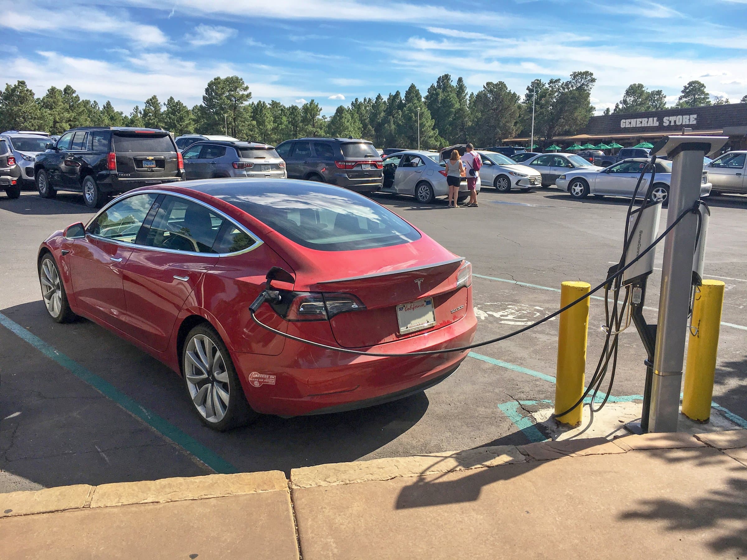 Red electric car plugged into a charging station beside yellow bollards in a sunny parking lot