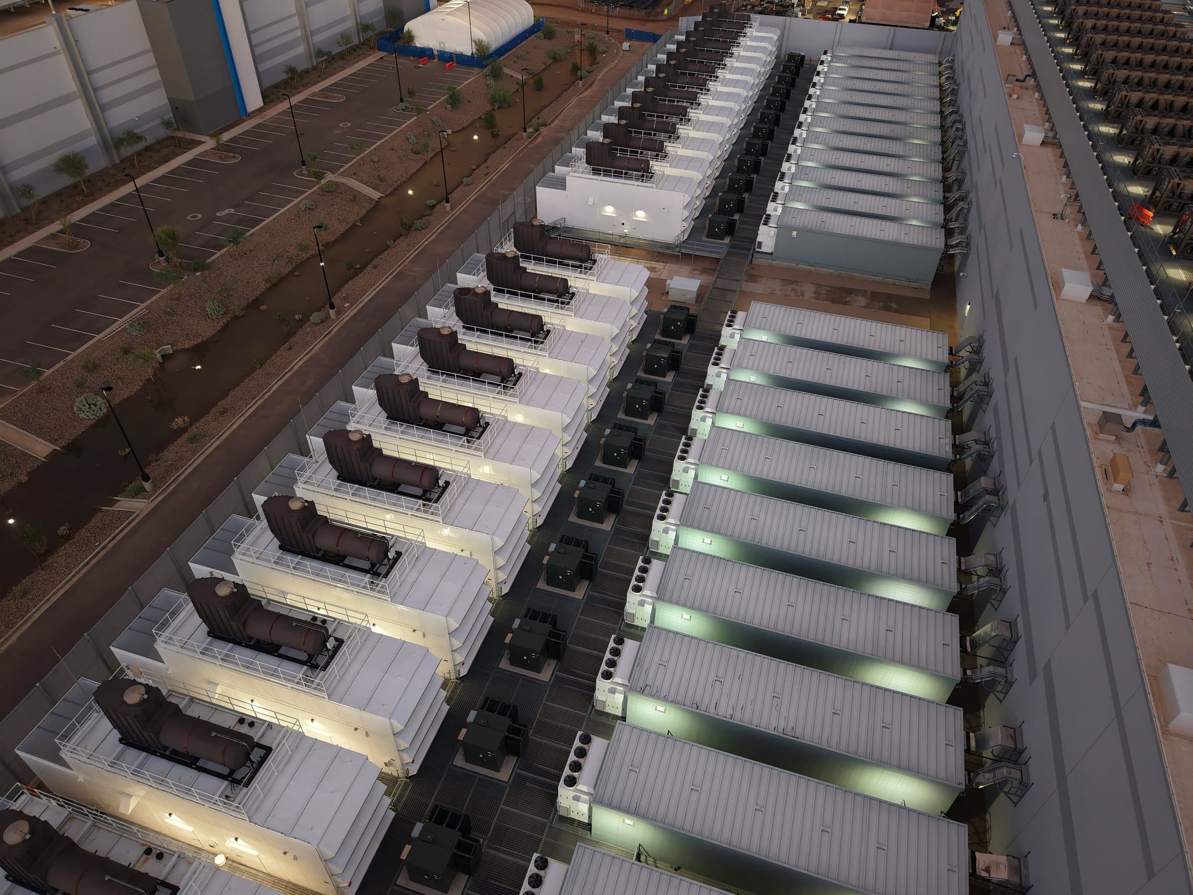 Aerial view of rows of backup generators with exhaust silencers beside a modern building at dusk