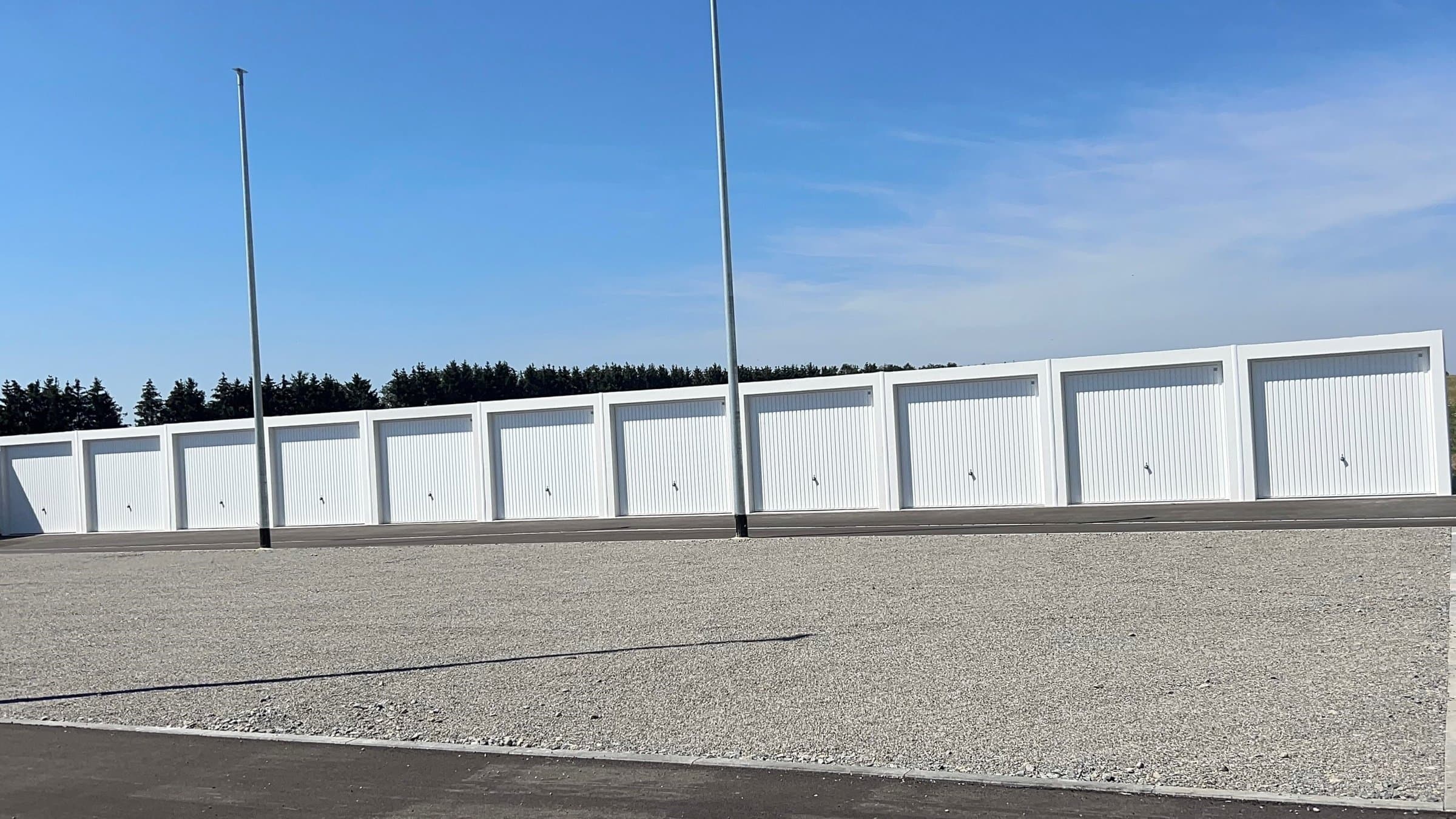 Row of white storage units with closed metal doors under a clear blue sky