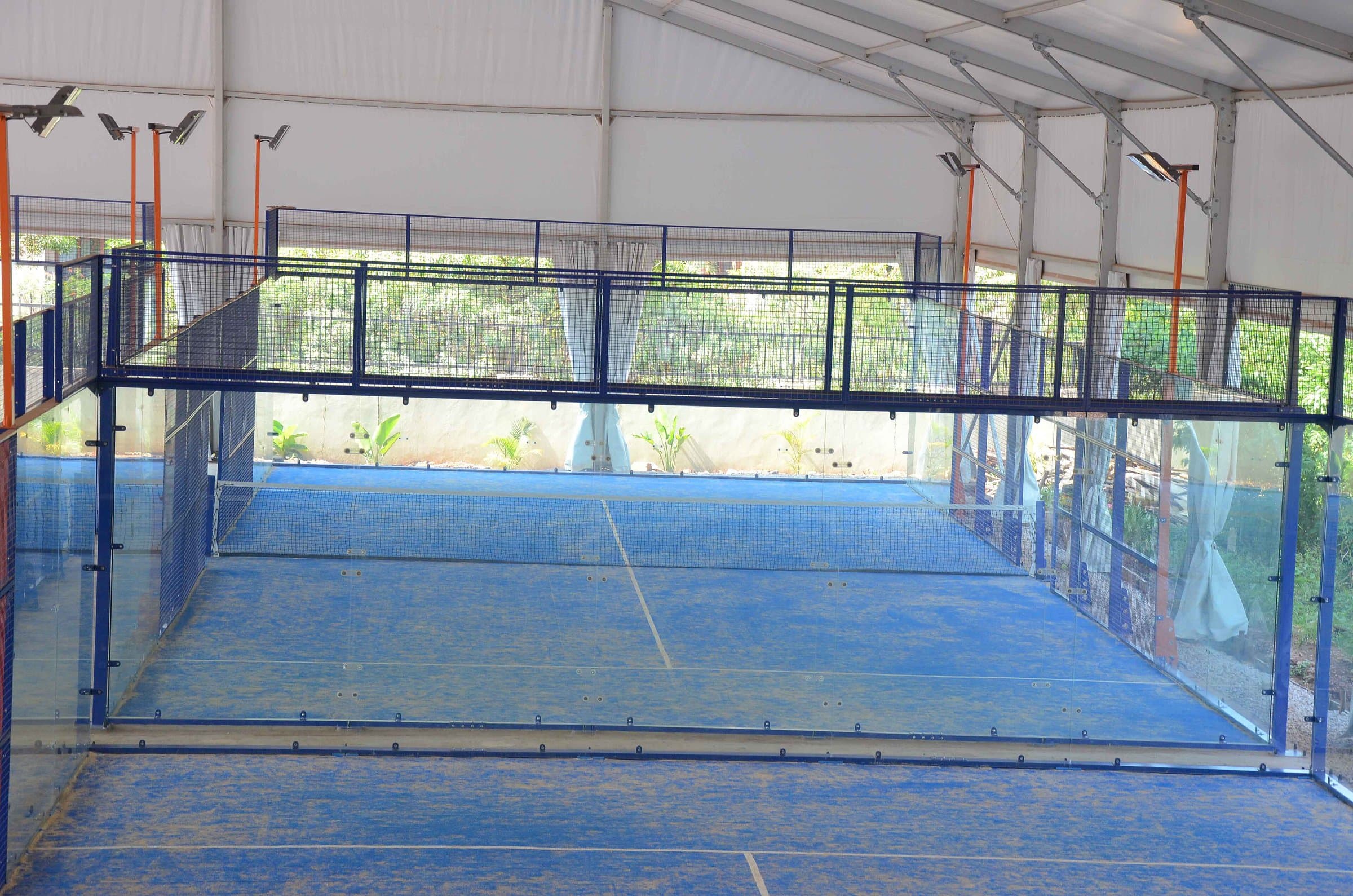 Empty covered padel court with blue turf, glass walls and a net under a white canopy