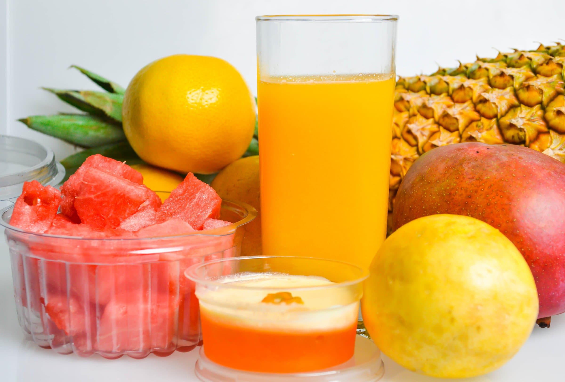 Tall glass of fresh juice surrounded by watermelon, mango, pineapple and citrus fruit