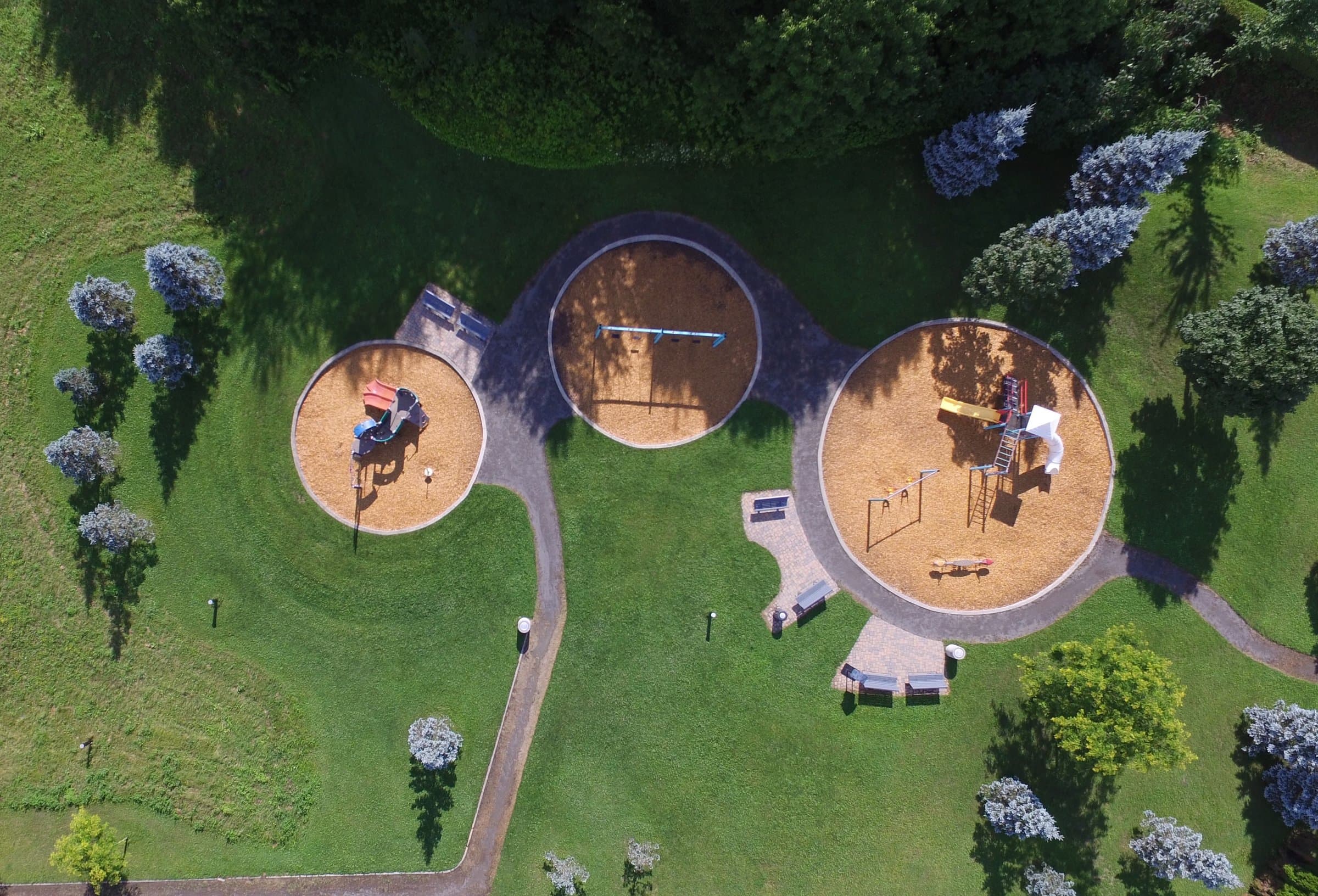 Aerial view of a kids playground with slides and swings in three round play areas on a green lawn