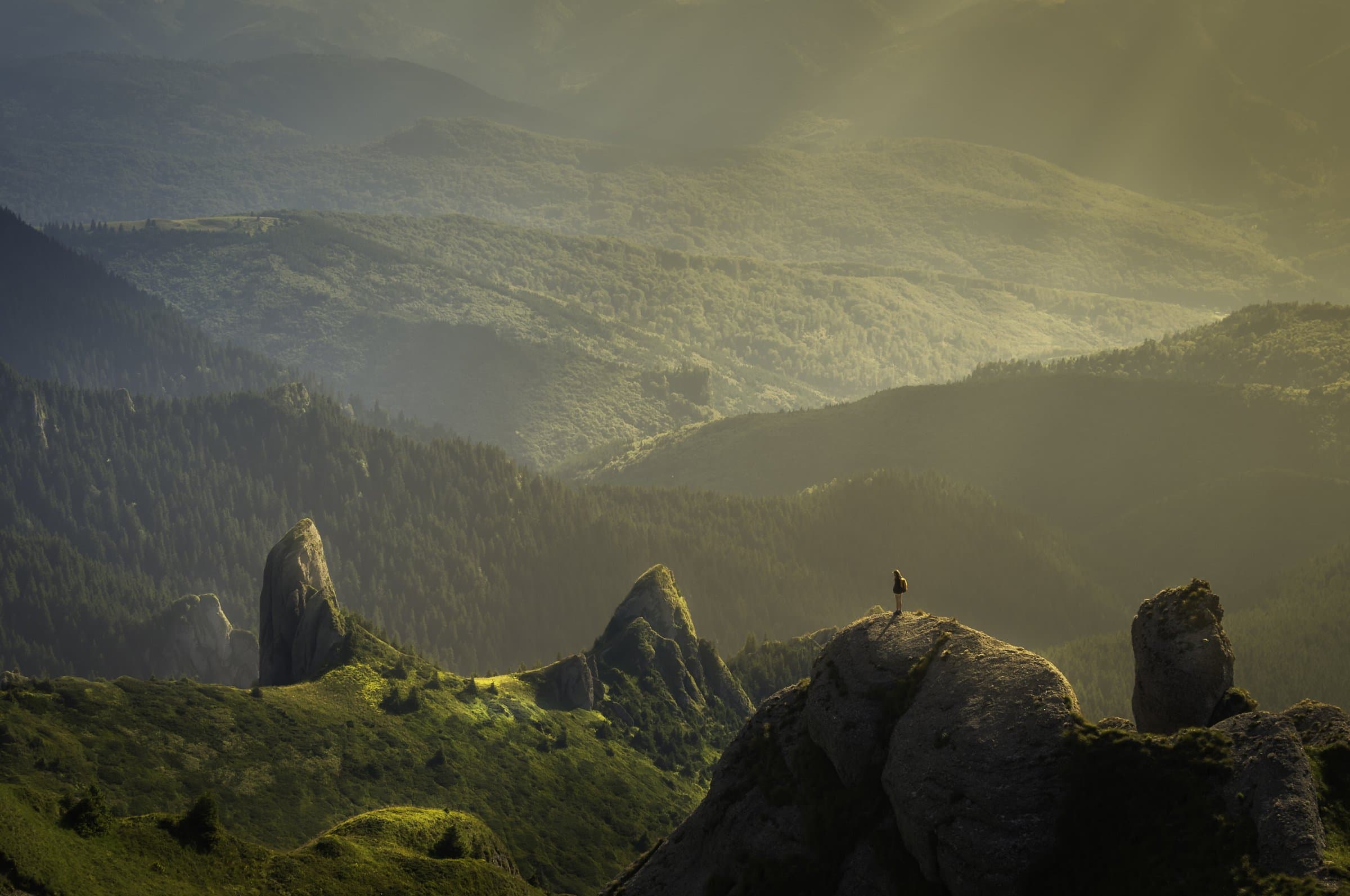 Green mountain ridges fading into golden haze above a valley with rocky outcrops