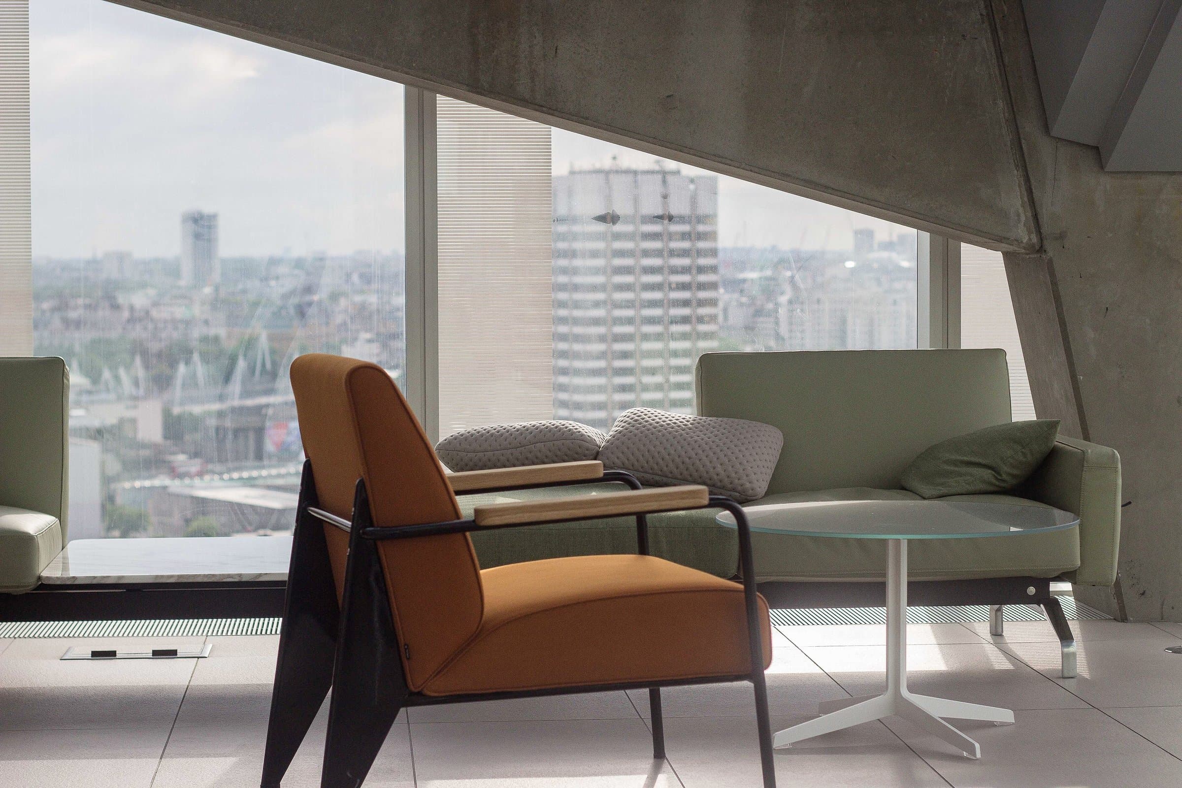 Lounge with armchairs beside floor-to-ceiling windows overlooking the city from a high floor