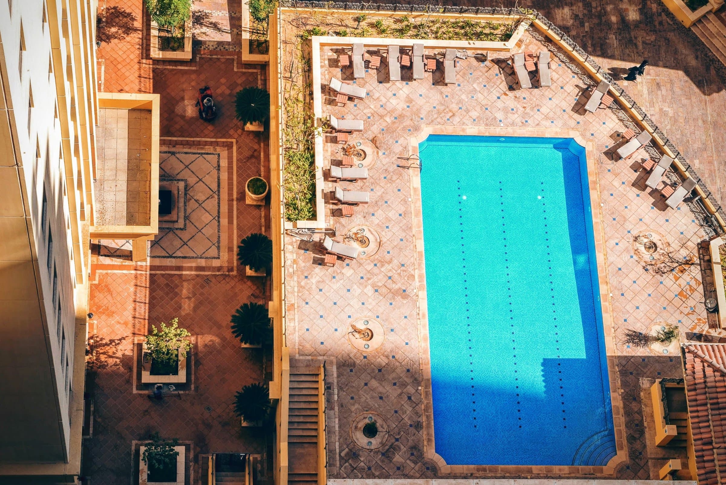 Aerial view of a turquoise swimming pool set in a terracotta-tiled deck with sun loungers
